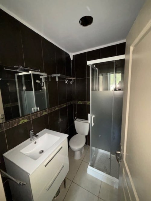 Salle de bains moderne avec carrelage noir, lavabo blanc, toilettes et douche vitrée à l'hôtel Le Clos Androne