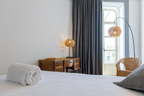 Quarto moderno na Aveiro com Paixão Living com cama branca, secretária de madeira, luminárias de vime e vista para a cidade