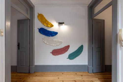 Arte de parede colorida com penas no corredor do apartamento de Aveiro com piso de madeira e portas cinzentas