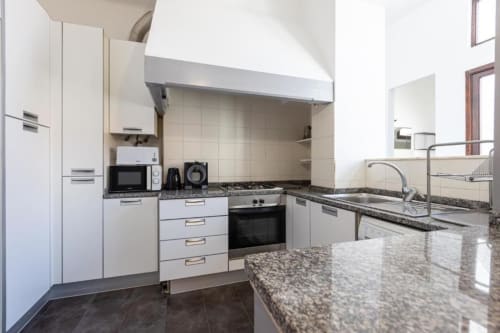 Cozinha moderna com armários brancos, bancadas em granito, eletrodomésticos integrados e pia em aço inoxidável no apartamento de Aveiro