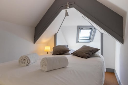Cozy attic bedroom at Aveiro com Paixão Living with bed, brown pillows, rolled towels, skylight window, and warm lamp