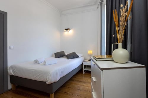 Quarto moderno em Aveiro com Paixão Living, cama branca, almofadas escuras, piso de madeira e decoração minimalista com plantas