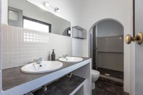 Banheiro compartilhado moderno com duplas pias, azulejaria branca, entrada de chuveiro arqueada e acabamentos em latão em Aveiro com