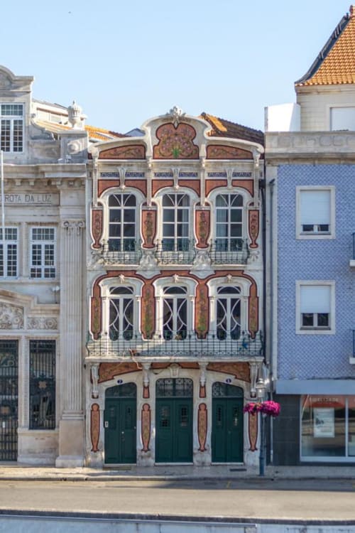 Historic Art Nouveau building facade in Aveiro, Portugal with ornate red tiles, decorative windows, and green doors