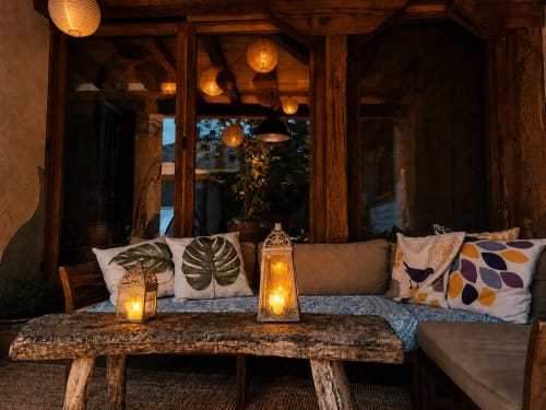 Salon cosy du soir à Viento de Ladera, Segovia avec sièges éclairés par des lanternes, coussins motifs, banc rustique et grandes fenêtres