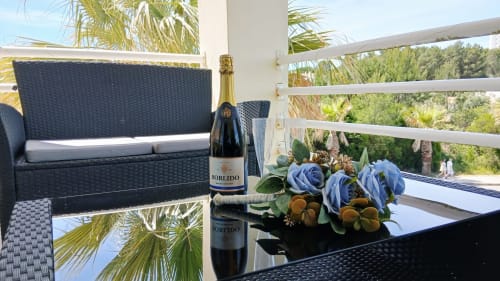 Elegante varanda do apartamento Sweet Home Amoreira em Portimão com sofá de rattan preto, flores azuis, champanhe e vista para o mar