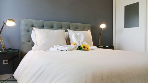 Quarto moderno do apartamento Sweet Home Amoreira em Portimão com lençóis brancos, cabeceira cinza e cisnes decorativos em toalhas