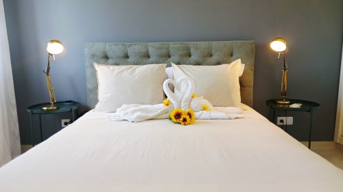 Quarto de luxo no Sweet Home Amoreira em Portimão com lençol branco, cisnes decorativos em toalha, girassóis e luminárias em latão