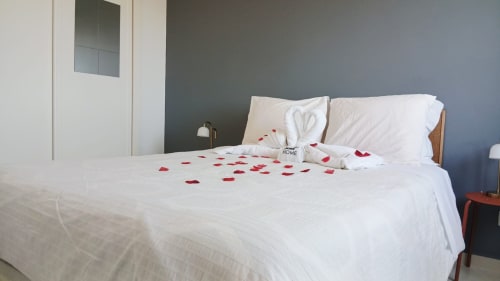 Quarto romântico no apartamento Sweet Home Amoreira em Portimão com pétalos de rosa vermelha espalhados sobre roupa de cama branca e decorativa