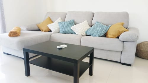 Sala de estar moderna com sofá cinza em L, almofadas azul e branco, mesa de centro preta e piso de madeira clara em Sweet