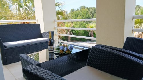 Terraço mobiliado com assentos em vime preto, garrafa de champanhe e flores com vista para as palmeiras em Sweet Home Amoreira