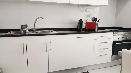 Cozinha moderna do apartamento Sweet Home Amoreira em Portimão, com armários brancos, bancada preta, pia e aço inoxidável