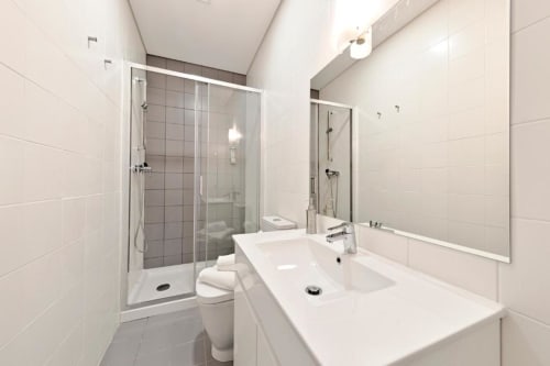 Banheiro moderno com dois lavatórios, box de vidro, vaso sanitário e espelho em apartamento no Porto