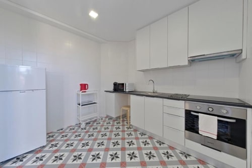 Cozinha moderna em apartamento no Porto com armários brancos, eletrodomésticos em aço inox e piso com azulejos decorativos