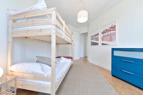 Spacious bedroom with wooden loft bed, blue dresser, and city views in Porto apartment