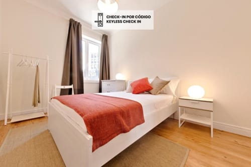 Quarto moderno com cama de casal, roupa de cama vermelha, criado branco, assoalho de madeira e vista para a cidade no apartamento do Porto