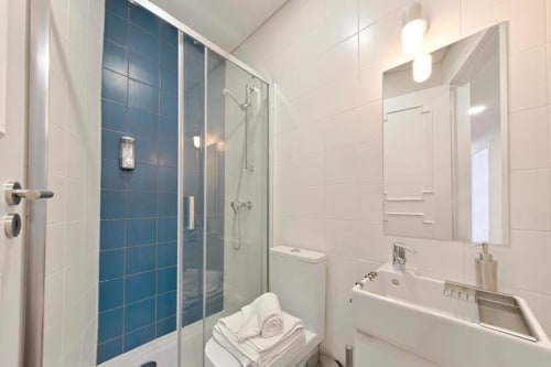 Banheiro moderno com chuveiro em azulejo azul, espelho, bancada branca e iluminação clara em apartamento no Porto