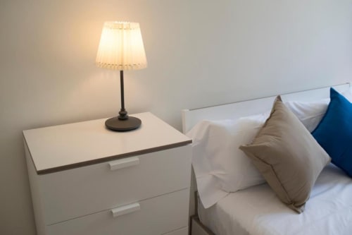 Criado-de-cama do quarto com luminária acesa ao lado da cama com almofadas no apartamento do Porto