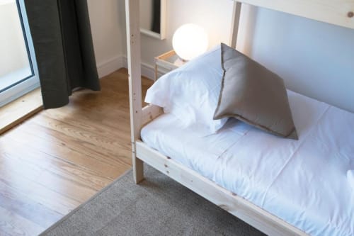 Quarto moderno em Aveiro com Paixão Living: cama com roupa branca, piso de madeira, luminária redonda e acesso à varanda com vista da cidade