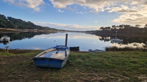 Bateau de pêche bleu sur berge herbeuse surplombant une rivière calme avec bateaux amarrés et rive boisée au Domaine De Millox