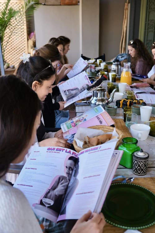 Women reading magazines at dining table during Riad 191 event in Marrakech