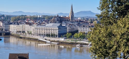 Paysage urbain fluvial français avec clocher gothique, montagnes et bâtiments classiques au bord de l'eau