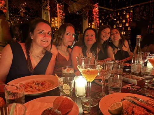 Five women dining together at Riad 191 in Marrakech, enjoying wine and pasta in an elegantly decorated restaurant with warm