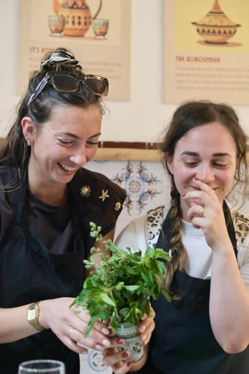 Two women smiling while holding fresh mint at Riad 191 Marrakech, enjoying traditional Moroccan hospitality experience.
