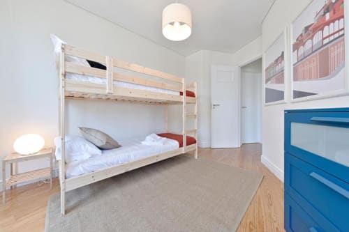 Bright bedroom with white bunk beds, wooden floors, blue dresser, and city view in Aveiro downtown apartment