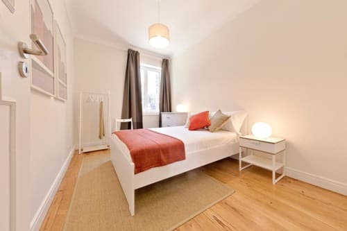 Modern bedroom at Aveiro com Paixão Living with white bed, coral bedding, wooden floors, and warm lighting in Portugal.