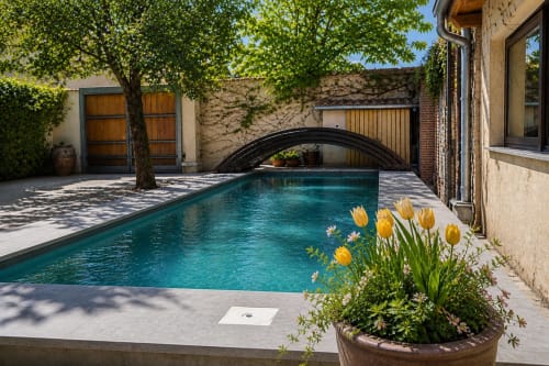 Patio de la piscine Viento de Ladera à Ségovie avec eau turquoise, voûte arquée, tulipes jaunes et architecture en pierre
