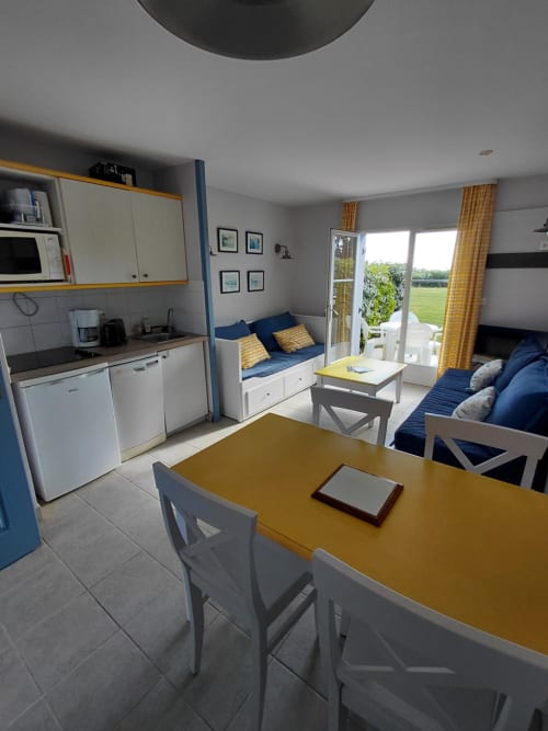 Appartement moderne à Loc'Maria Belle Île avec table à manger jaune, cuisine blanche, coin salon bleu et accès à la vue mer