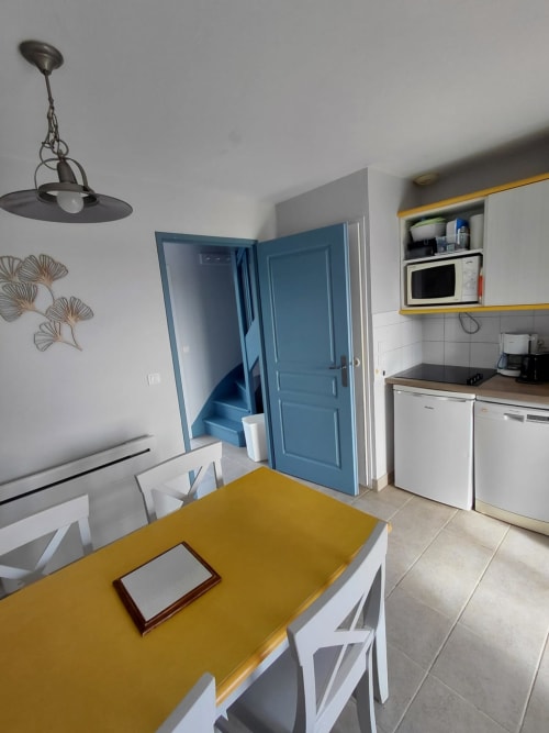Cuisine et salle à manger modernes dans un appartement de Belle Île-en-Mer avec table jaune, portes bleues et électroménagers blancs