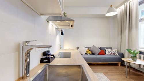 Modern studio apartment at tARTu Stays with open kitchen, sink, dining area, gray sofa with pillows, and city view through