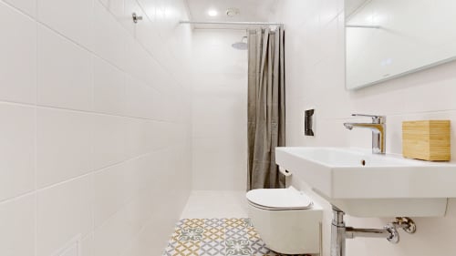 Modern bathroom in tARTu Stays apartment with white tiles, shower, toilet, sink, wooden storage, and patterned floor