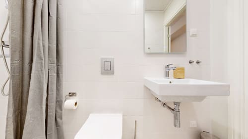 Modern bathroom in tARTu Stays apartment featuring white sink, toilet, shower with beige curtain, and wall-mounted mirror in