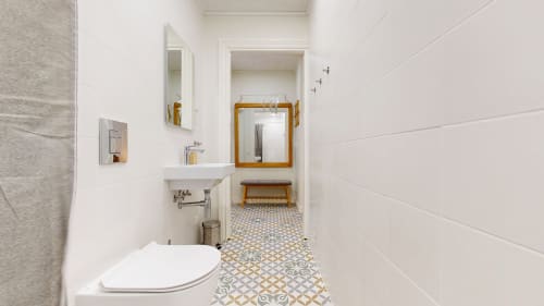 Modern bathroom in tARTu Stays apartment with white tiles, patterned floor, sink, toilet, and wooden-framed mirror in Tartu