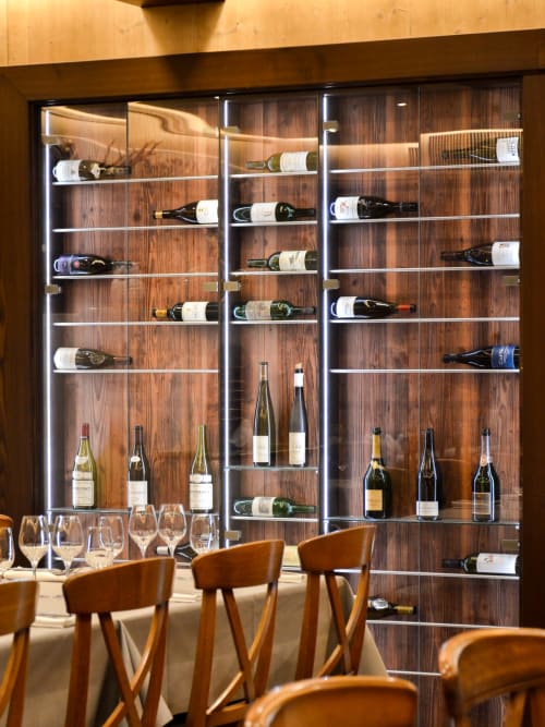 Élégante vitrine de vin avec étagères illuminées à l'Hôtel Des Vosges, Sommerau, présentant bouteilles et verres.