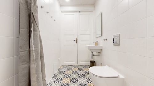 Modern bathroom at tARTu Stays with patterned tile floor, white tiles, sink, toilet, and gray towel