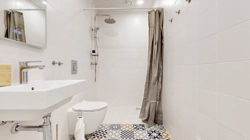Modern bathroom at tARTu Stays with white tiles, pedestal sink, shower, toilet, and patterned floor