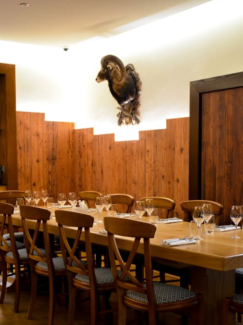 Élégante salle à manger de l'Hôtel Des Vosges avec table en bois, chaises, couverts et tête de bélier empaillée.