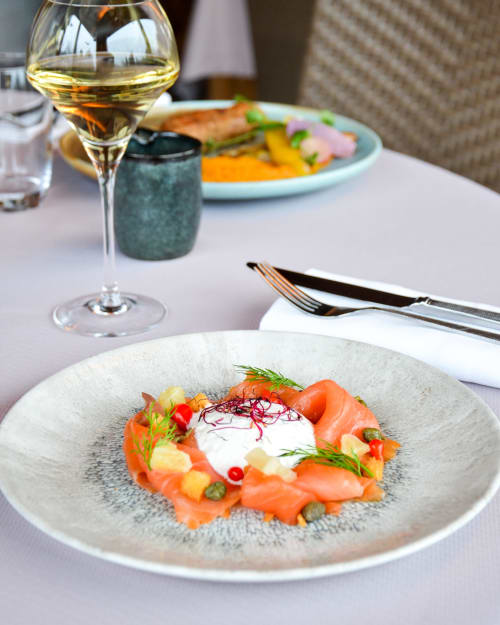 Élégant saumon présenté en assiette avec crème blanche et pousses fraîches à l'Hôtel Des Vosges, accompagné d'un vin blanc