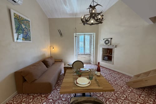 Okzitanisches Heritage-FerienStudio in Aiguèze, einem der schönsten Dörfer Frankreichs nahe den Ardèche-Schluchten, mit Bademöglichkeit im Fluss, Zugang zu Fuß, mit orangefarbenem Sofa, antiken Zementfliesen, Blick auf das historische Zentrum, Esstisch, verziertem Teppich und antiker Dekoration.