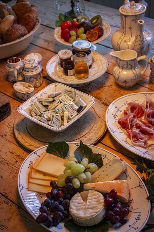 Elegant breakfast spread at Castanea Business & Suites with cheese, cured meats, grapes, and blue-and-white porcelain