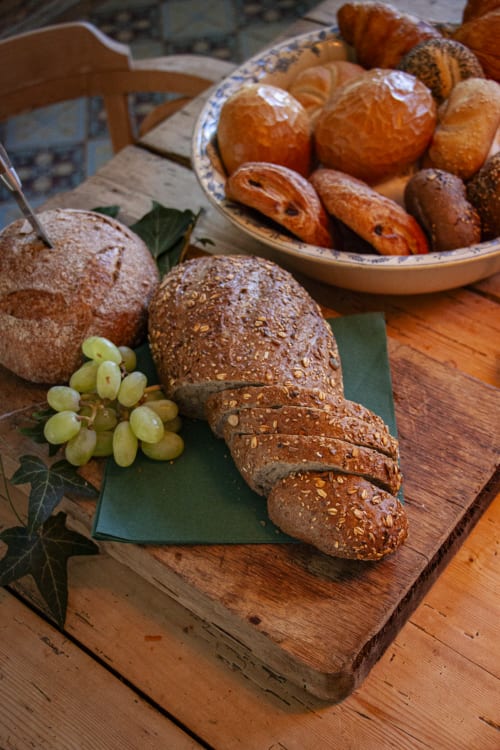 Fresh seeded bread, pastries, and grapes on wooden board at Castanea Business & Suites in Merelbeke