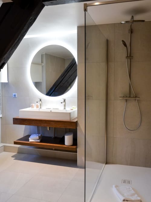Salle de bain moderne de l'Hôtel Des Vosges Sommerau avec miroir rond illuminé, meuble-lavabo en bois et douche à l'italienne