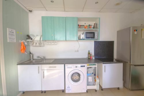 Cucina in comune dell'Hostel Tropical Work a Las Palmas con armadi turchesi, lavatrice, lavandino e microonde