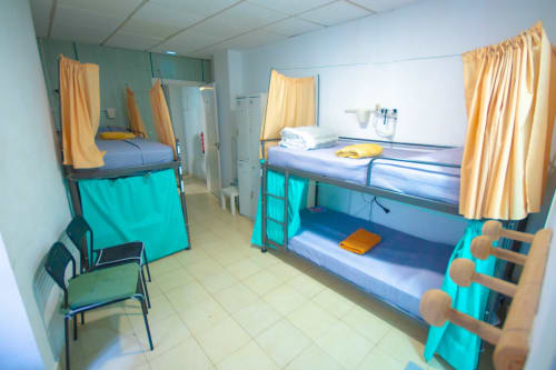 Camera dormitorio condivisa con quattro letti a castello, tende gialle e storage turchese presso l'Hostel Tropical Work di Las Palmas