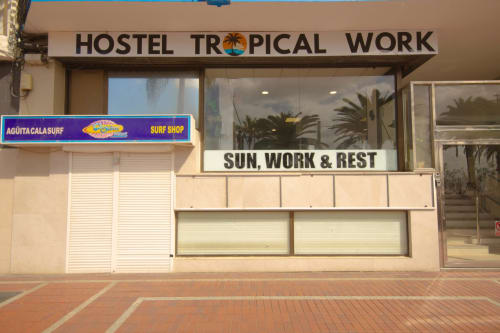 Vetrina dell'ostello Hostel Tropical Work a Las Palmas de Gran Canaria con riflessi di palme e insegna di negozio di surf