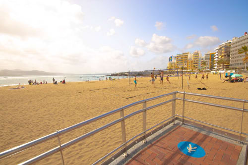Vista della spiaggia di lavoro dell'Hostel Tropical a Las Palmas de Gran Canaria con sabbia, reti da pallavolo e lungomare giallo